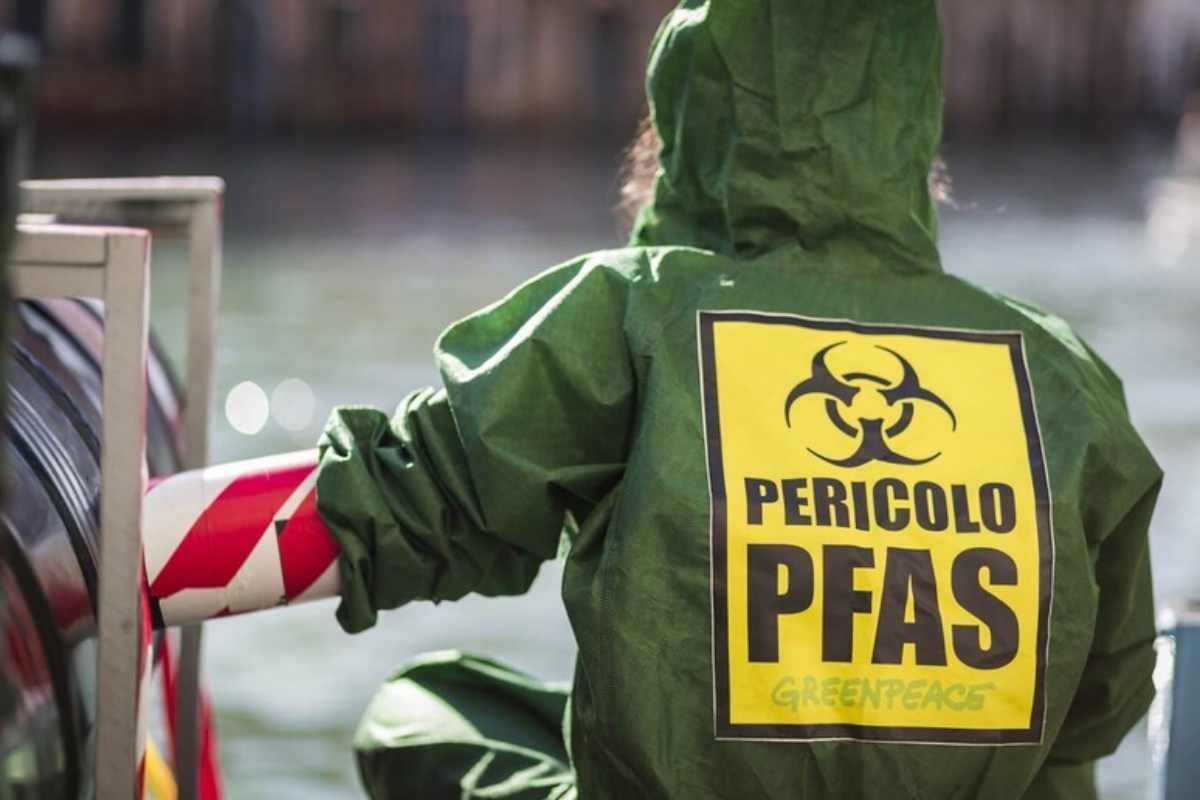 Una parsona con la tuta di Greenpeace e la scritta "Pericolo PFAS"