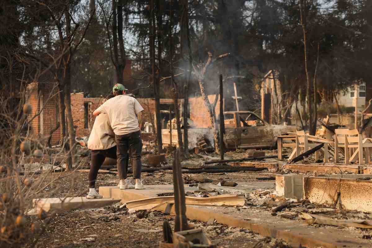 Coppia abbracciata davanti ai resti della loro casa devastata dalle fiamme a Los Angeles