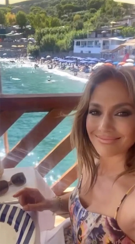 Jennifer Lopez sorridente al tavoli di un ristorante sullo sfondo di Capri