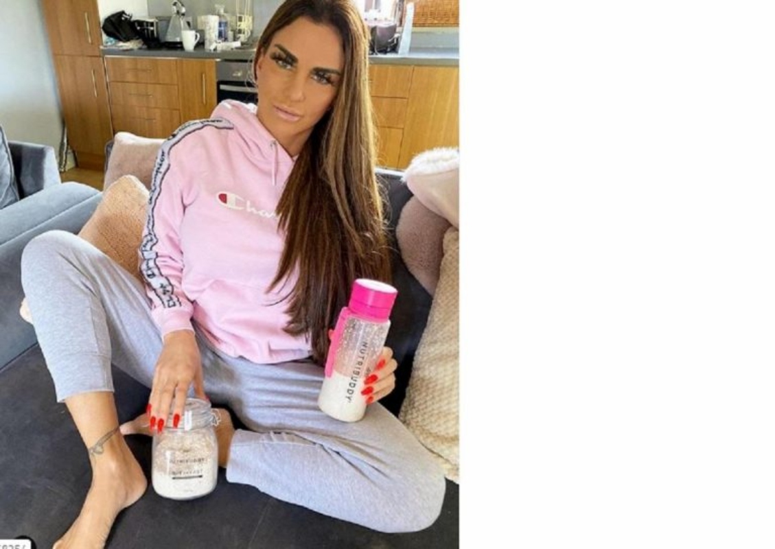 Katie Price in poltrona in tuta rosa e grigia con i suoi prodotti di bellezza