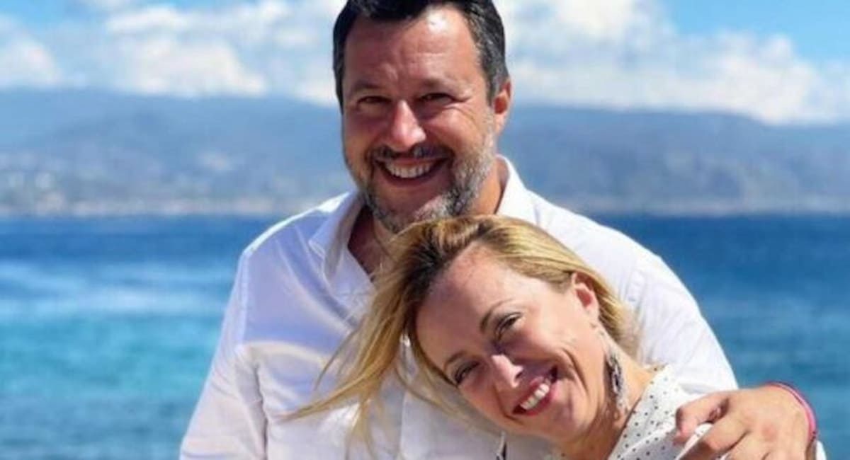 Salvini e Neloni abbracciati sullo sfondo di un golfo.