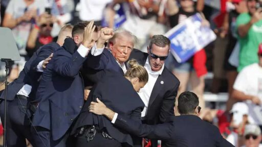 Donald Trump ferito, col sangue che gli cola dall'orecchio, sostenuto dagli agenti, col pugno alzato