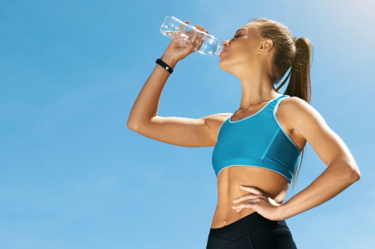 donna atletica beve acqua da una bottiglia