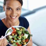 donna sorridente con una ciotola di insalata mista in mano come esempio della dieta mangia tutto