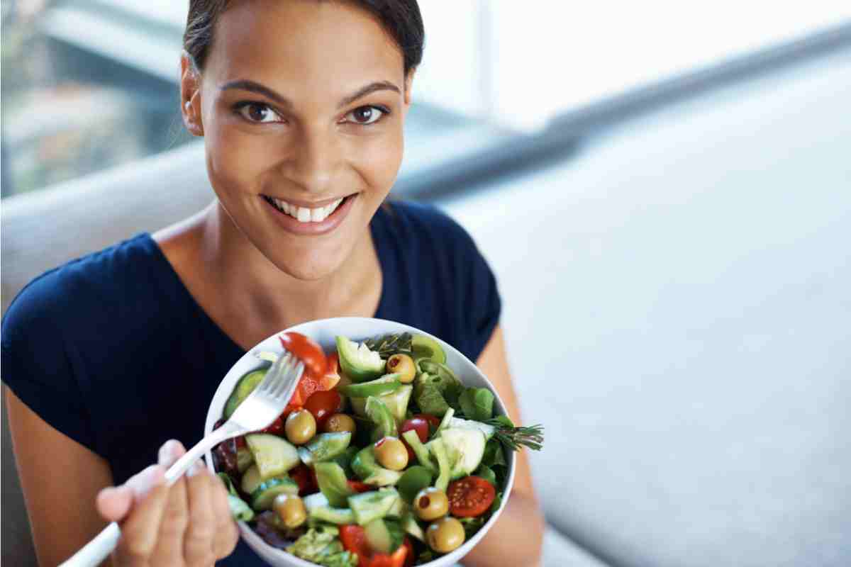 donna sorridente con una ciotola di insalata mista in mano come esempio della dieta mangia tutto