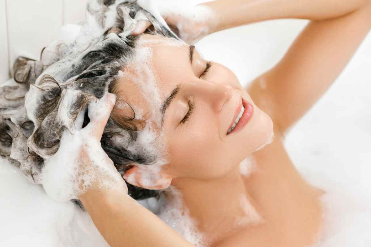 donna lava i capelli con lo shampoo immersa in una vasca da bagno