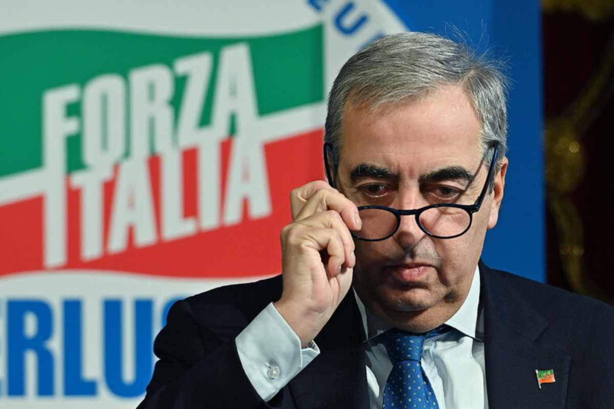 Maurizio Gasparri davanti alla bandiera di Forza Italia mentre si toglie gli occhiali