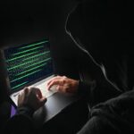 Hacker in azione con il suo computer, in una stanza illuminata solo dal monitor