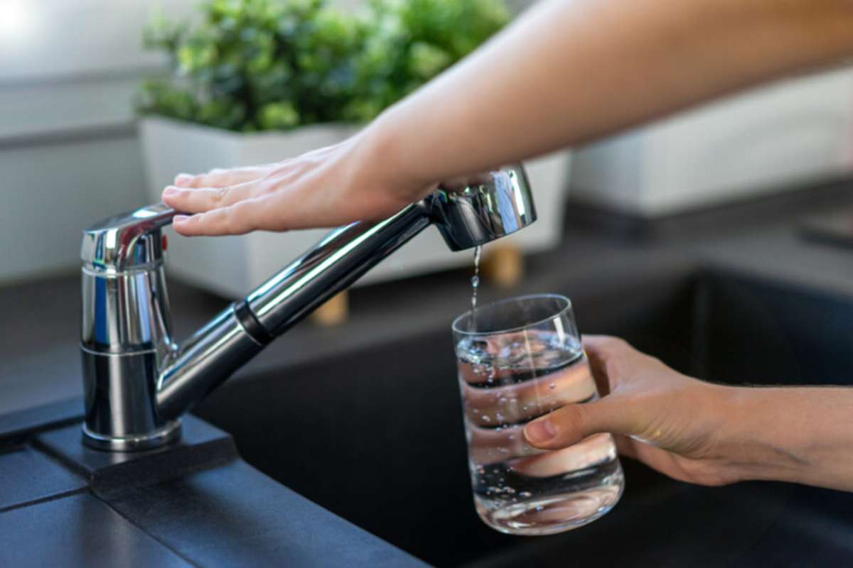 Una donna riempie un bicchiere d'acqua dal ribunetto di casa