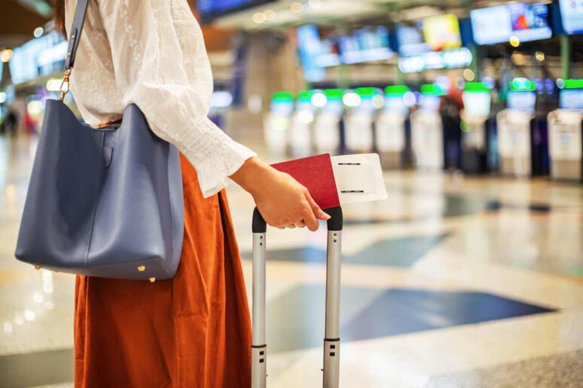 Una donna all'aeroporto di profilo con un trolley e la carta d'imbarco in mano