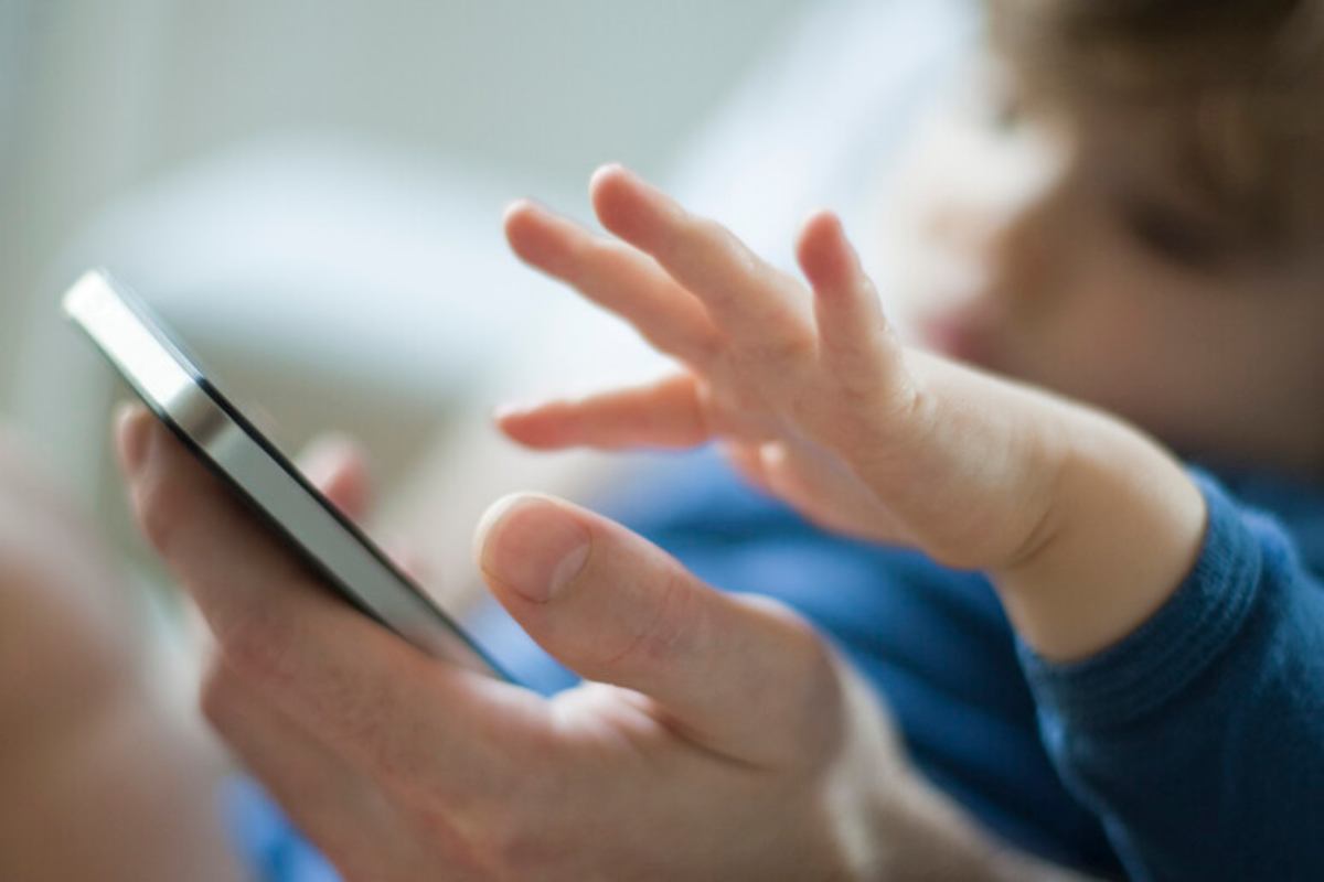 La mano di un adulto e quella di un bambino vicino alla schermo di un cellulare