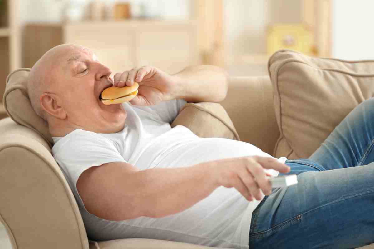 uomo mangia un panino sdraiato sul divano