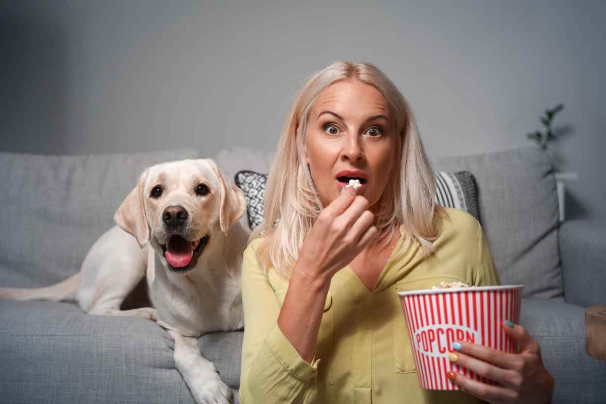 donna mangia popcorn davanti a un film con dietro un cane sul divano