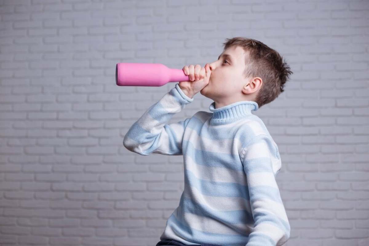 un bambino fa finta di bere da una bottiglia