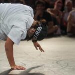 uomo con berretto nero che fa breakdance con pubblico in sala