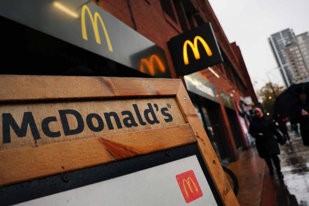 In primo piano un'insegna di legno di McDonald's, sullo sfondo un loro punto vendita