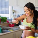 una ragazza fa colazione in cucina con dello yogurt e frutta