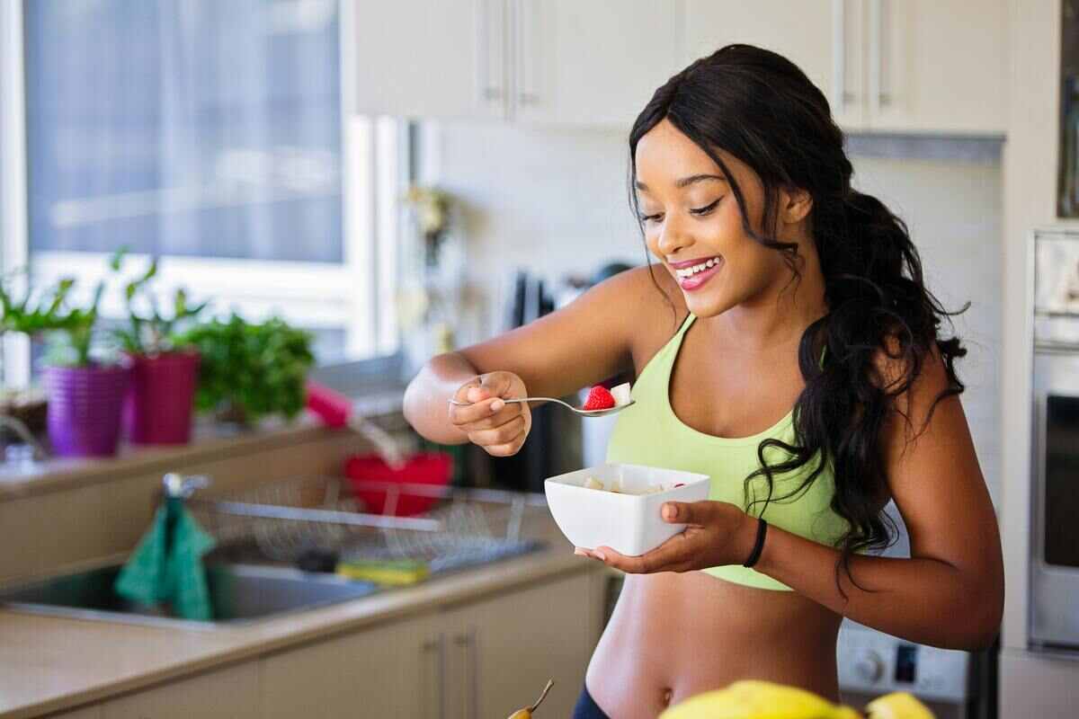 una ragazza fa colazione in cucina con dello yogurt e frutta