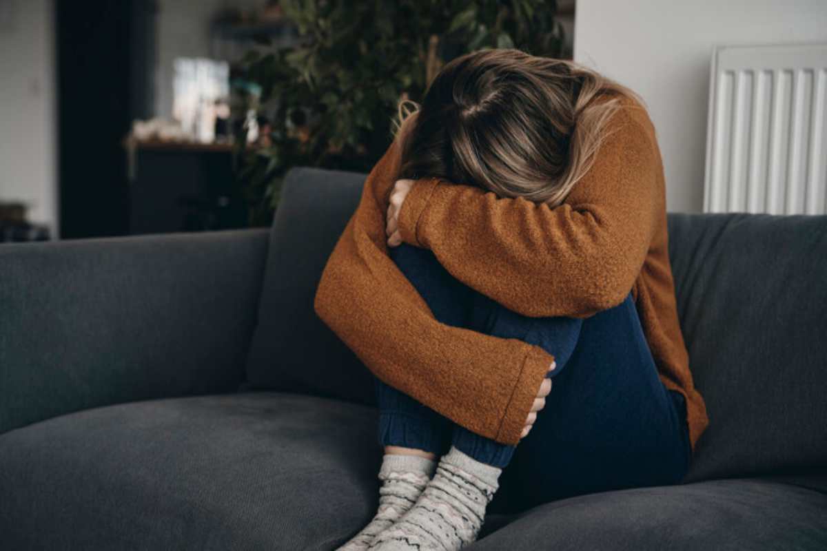 Una donna triste sul divano con la testa tra le braccia, poggiata sulle gambe