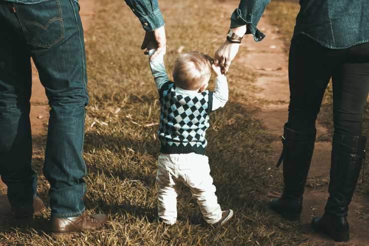 Un bambino piccolo passeggia dando la mano ai genitori