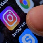 L'icona di Instagram in evidenza sullo schermo di un cellulare e il pollice di una persona accanto