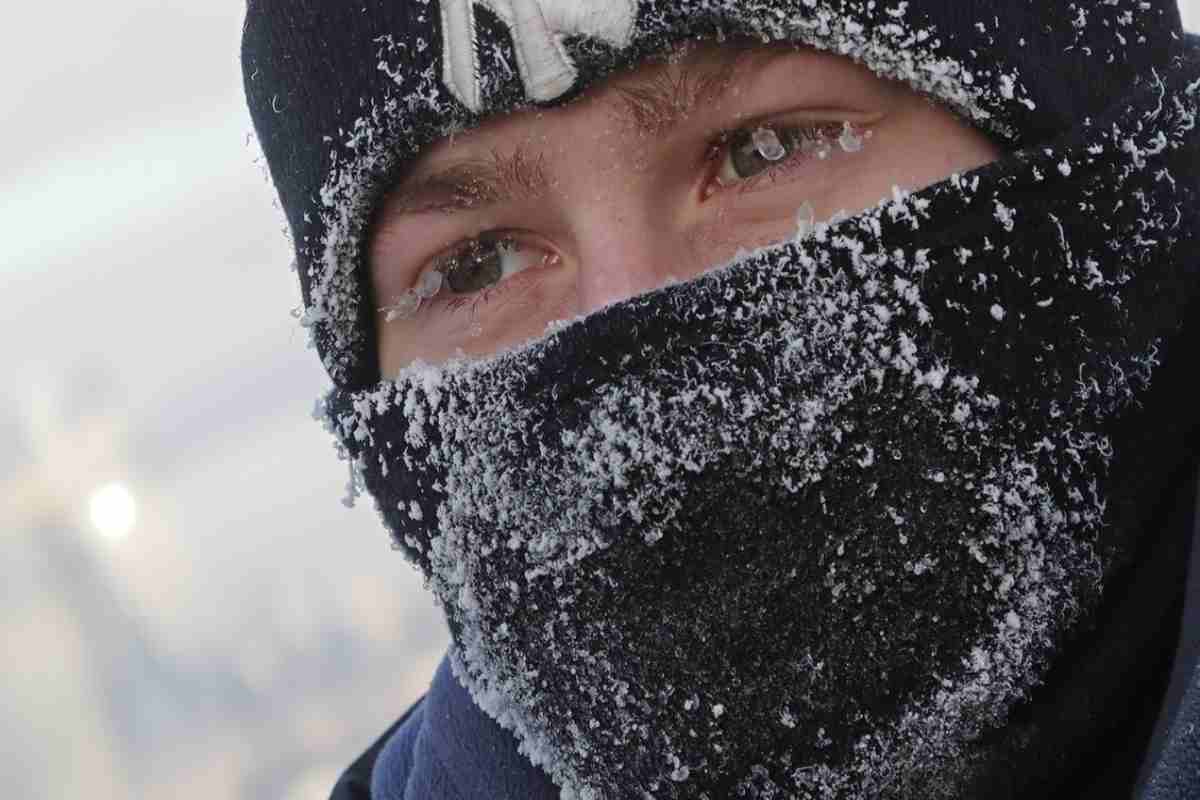 Primo piano di un uomo che si ripara dalla neve, con cappello e una sciarpa sul viso 