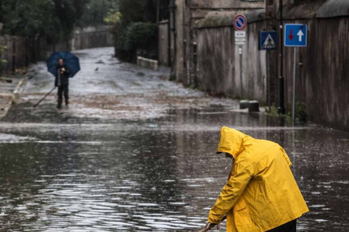 uomo con imbermeabile spala l'acqua dopo un nubifragio