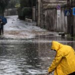 persona cerca di far confluire l'acqua nei tombini dopo un nubifragio