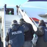 Alcuni poliziotti portano a bordo di un aereo un migrante da rimpatriare