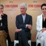 Il cast del film Eterno visionario nel corso di un'intervista, sullo sfondo la locandina del film