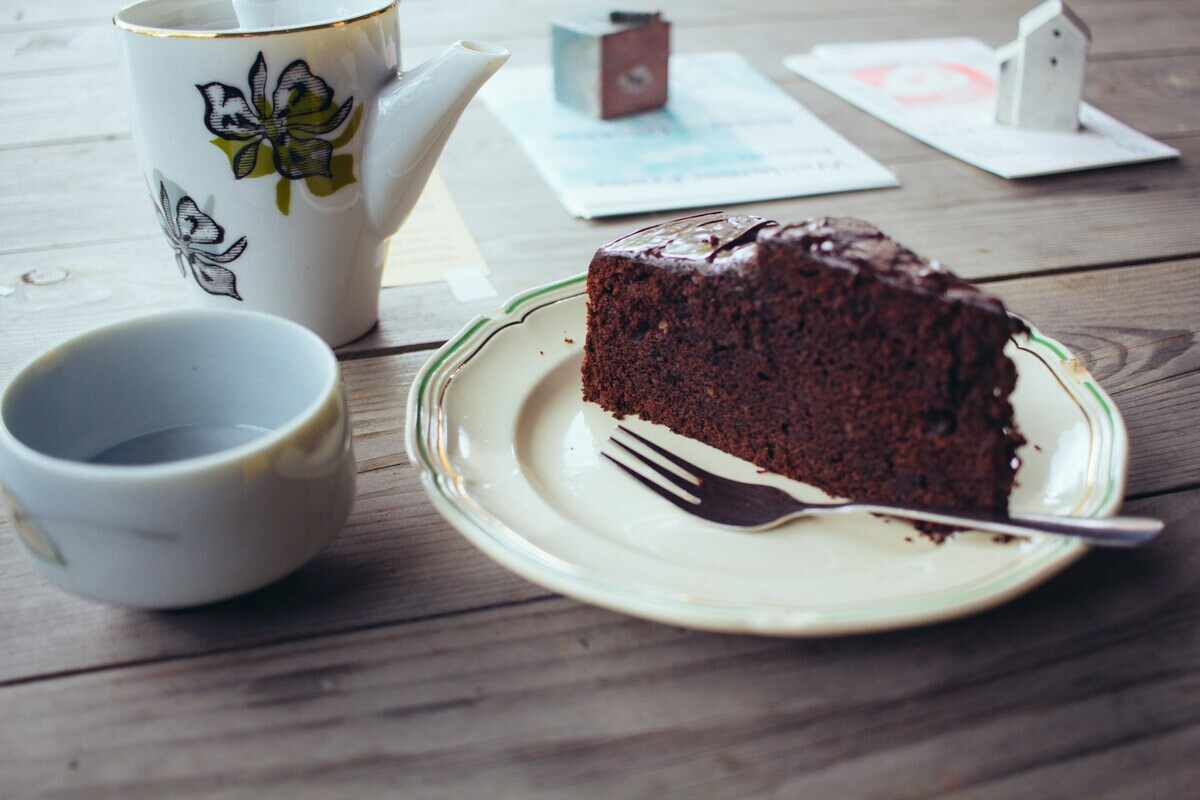 una fetta di torta al cioccolato su un piattino acompagnata da una tazza di té