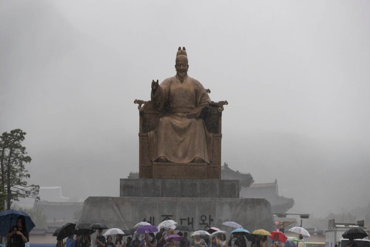 Statua di Sejong il Grande in Corea del Sud e diversi visitatori con l'ombrello, in una giornata di pioggia