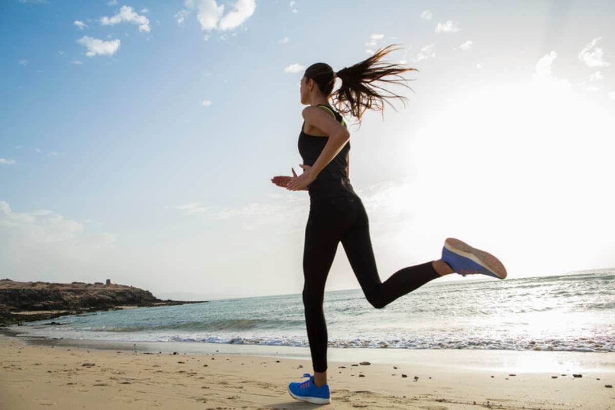 Una donna fa esercizio sulla spiaggia correndo in riva al mare