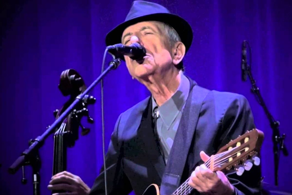 Leonard Cohen al microfono e con la chitarra in mano durante un'esibizione