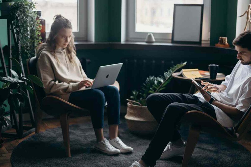 due ragazzi stanno seduti e lavorano al pc e al cellulare