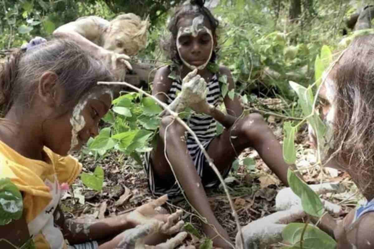 Un gruppo di bambine aborigene australiane, sedute in mezzo alla vegetazione