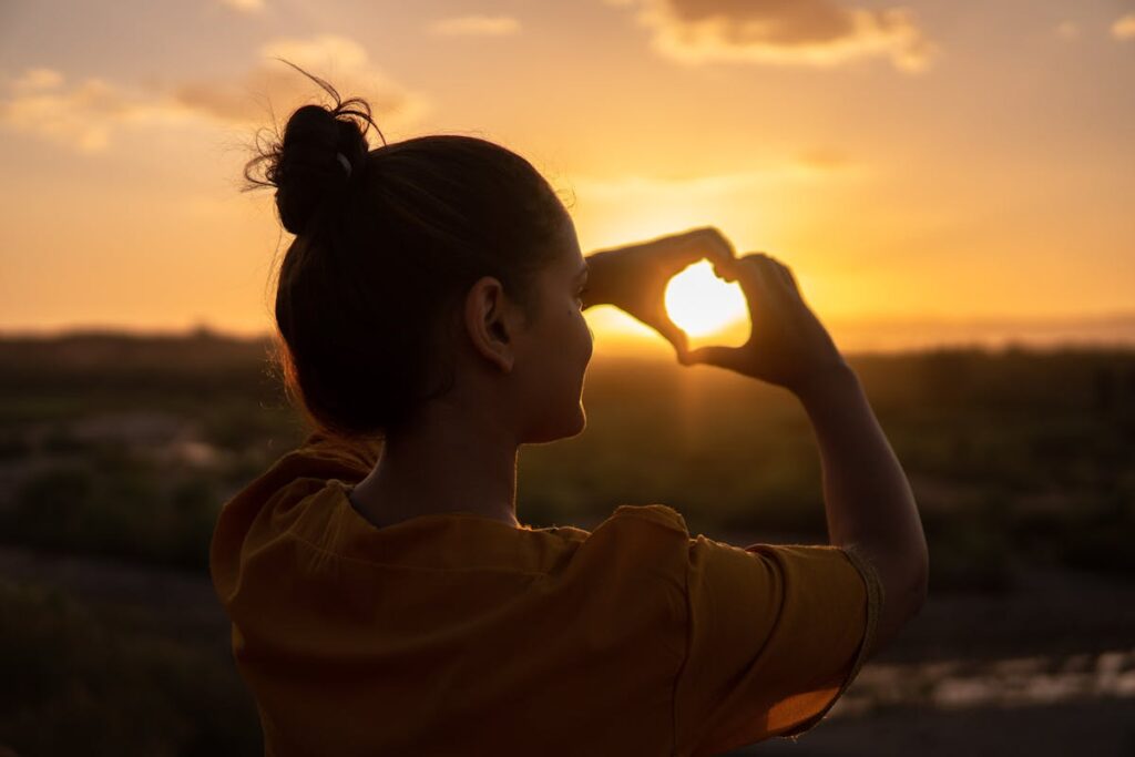 una ragazza fa un cuore al sole al tramonto