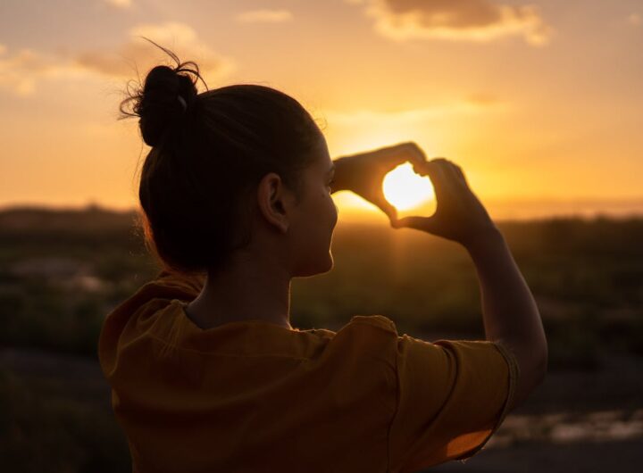 una ragazza fa un cuore al sole al tramonto