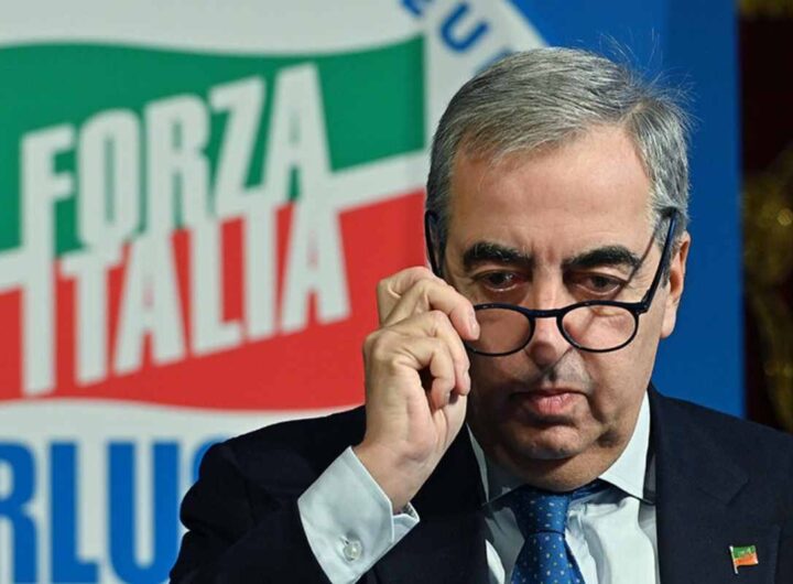 Maurizio Gasparri mentre si toglie occhiali davanti bandiera Forza Italia