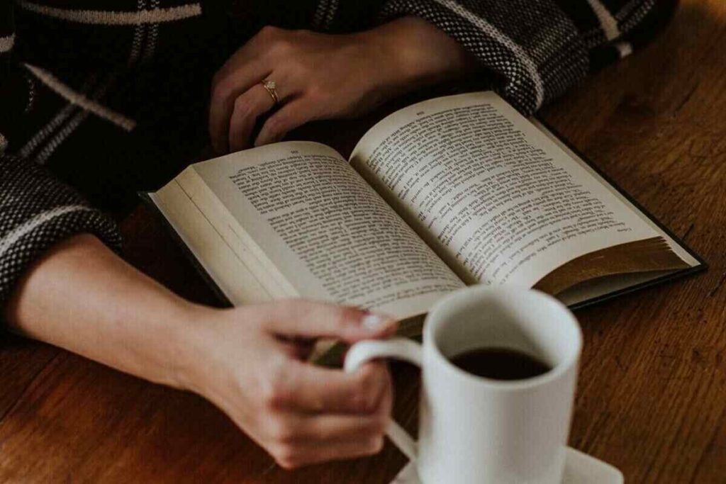 una perosna beve caffè mentre legge un libro