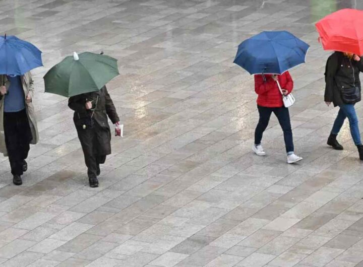 Ombrelli aperti, gente passeggia sotto la pioggia