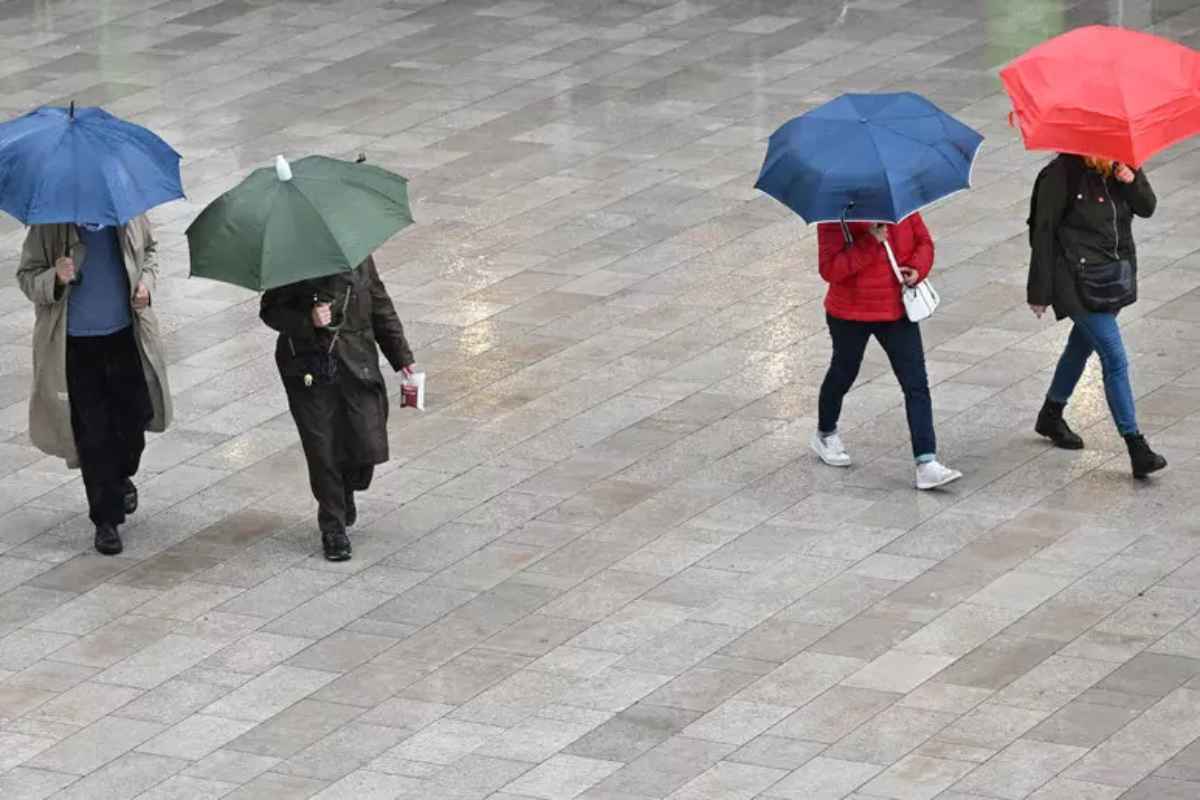 Persone camminano sotto la pioggia con l'ombrello aperto